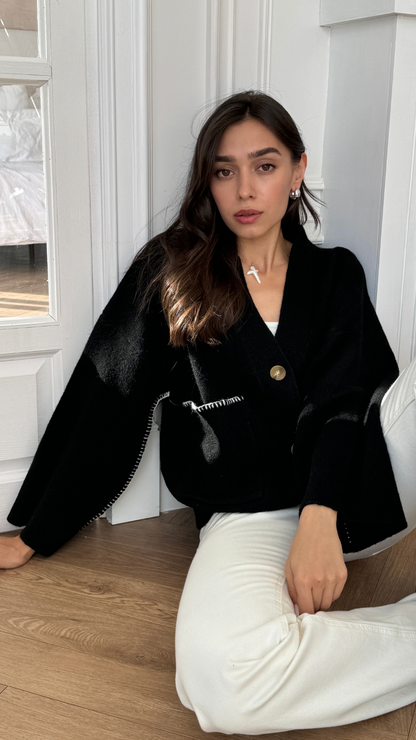 black oversized cardigan with a large button and white stitching details, paired with white trousers